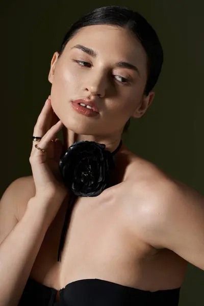 stock image A young woman with brunette hair poses against a black background, wearing a black rose choker.