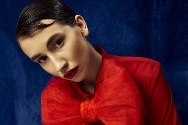 A young woman with short hair poses in a red shirt with a large bow against a blue backdrop. clipart