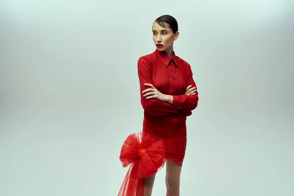 stock image A young woman with short hair poses in a red dress and bow against a grey background.