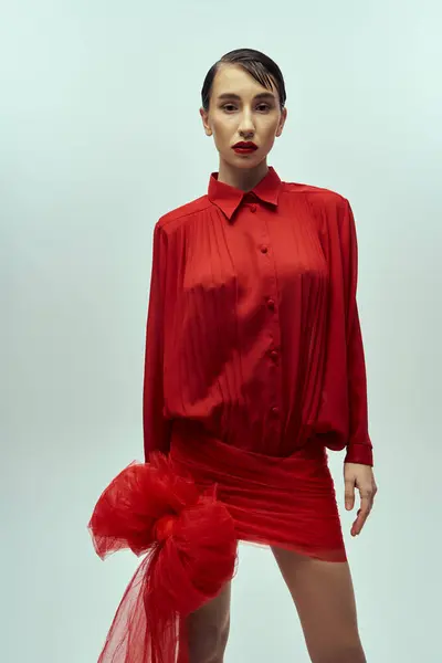 stock image A young woman with short hair models a red dress with a bow against a grey backdrop.