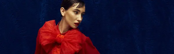 stock image A young woman with short hair poses in a vibrant red outfit against a rich blue backdrop.