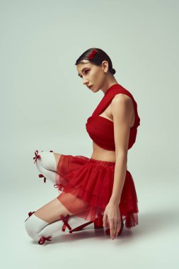 Güzel bir genç kadın gri bir arka plana karşı beyaz dantelli kırmızı bir bluz ve mini etekle poz veriyor..