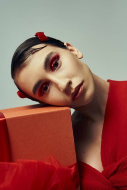 A beautiful young woman with short hair wears a red outfit and a bow while holding a present in a studio setting. clipart