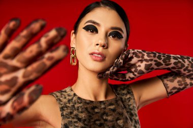 A young woman with bold makeup and leopard print gloves poses for a fashion photo shoot. clipart