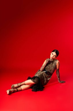 Şık giyinmiş genç bir kadın kırmızı bir stüdyoda poz veriyor..