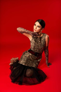 Leopar desenli elbise giymiş genç bir kadın kırmızı arka planda poz veriyor..