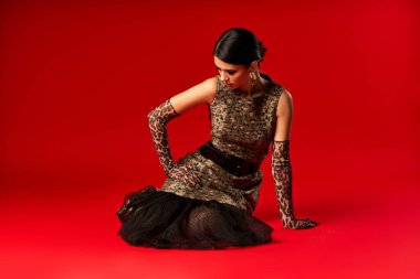 Leopar desenli elbise giymiş genç bir kadın kırmızı arka planda poz veriyor..