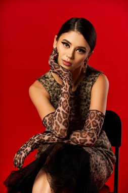 A young woman in a leopard print dress and gloves poses confidently against a red backdrop. clipart