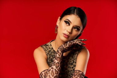 A young woman in a leopard print dress and gloves poses against a red background. clipart