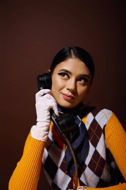 Süveter giymiş şık bir kadın klasik bir telefondan konuşuyor..