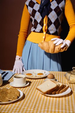 Genç bir kadın kahvaltı masasında kruvasan sunuyor. Yumurta, ekmek, kahve....