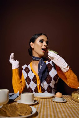 A stylish woman in a patterned sweater sits at a table, enjoying a snack. clipart