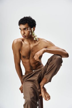 Genç, kaslı bir Afrikalı Amerikalı vücudunda ve yüzünde çiçeklerle gri bir arkaplanda poz veriyor..