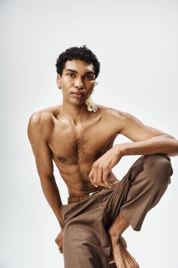Çiçeklerle süslenmiş kaslı bir Afrikalı genç adam gri bir zemine karşı güvenle poz veriyor..