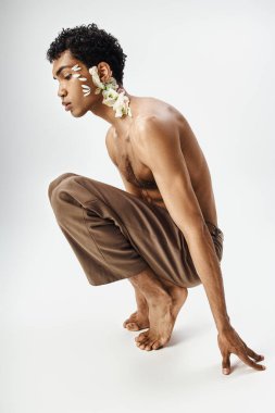 Vücudunda ve yüzünde çiçekler olan genç, kaslı bir Afrikalı Amerikalı adam gri bir arka plana karşı duruyor..
