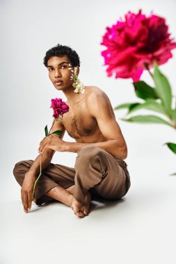 Genç ve kaslı bir Afrikalı Amerikalı vücudunda ve yüzünde çiçeklerle gri bir arkaplanda poz veriyor..