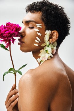 A young, muscular African American man poses with flowers adorning his body and face against a grey backdrop. clipart