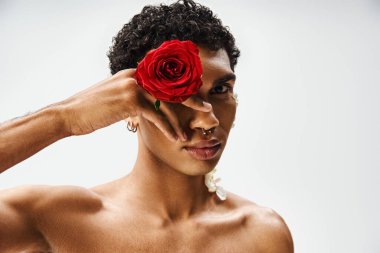 Genç, kaslı Afrikalı Amerikalı bir adam yüzünde ve vücudunda çiçeklerle gri bir arkaplanda poz veriyor..