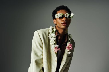 A young African American man poses in a light blazer adorned with flowers, his face framed by a floral-shaped eyewear. clipart