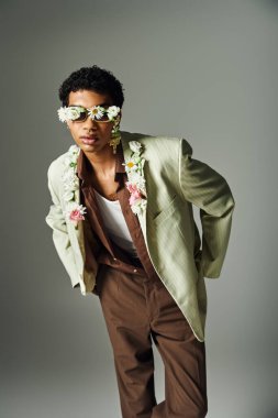 Süslü ceketli genç bir Afrikalı Amerikalı boynunu ve yüzünü süsleyen çiçeklerle poz veriyor, güzellik ve çeşitlilik sergiliyor..