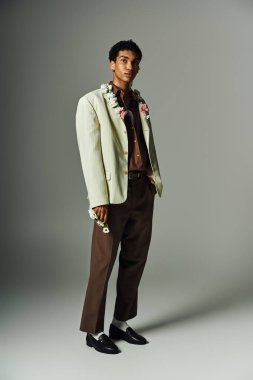 Kendine güvenen, şık bir ceketi olan, çiçek takan genç bir zenci, basit bir gri arka plana karşı duruyor, güzelliğini sergiliyor..