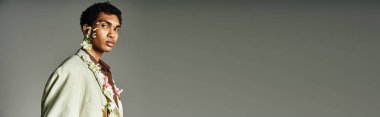 Gri bir zemine karşı şık ceketli genç bir zenci poz veriyor. Boynunda ve yüzünde çiçekler Güzelliği ve çeşitliliği vurguluyor.