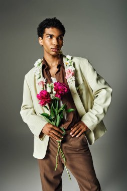 A young Black man looks stylish in a cream blazer, brown pants, flower garland, and bouquet of pink flowers. clipart