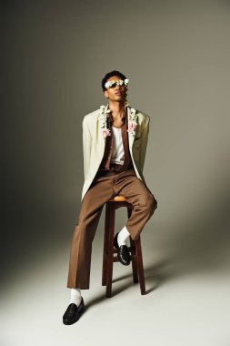 Genç Afrikalı Amerikalı bir adam şık bir ceketle poz veriyor. Boynunda çiçekler var.