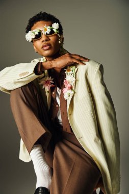 A young African American man poses in a cream blazer, accented with flowers around his neck and face. clipart