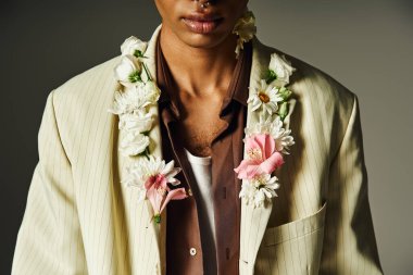 Çiçeklerle süslenmiş şık ceketli genç Afrikalı Amerikalı bir adam gri bir arkaplanda poz veriyor..