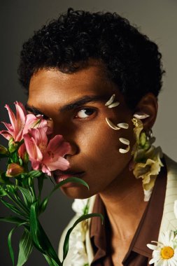 Genç bir siyah adam şık bir ceketle poz veriyor. Yüzünde çiçekler var.