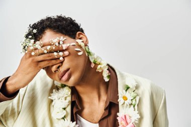 Genç bir Afrikalı Amerikalı, gri bir arka planda yüzünü ve boynunu süsleyen çiçeklerle poz veriyor..