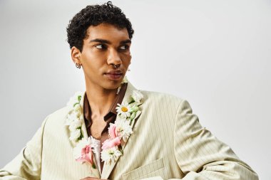 A young African American man with flowers around his neck and face poses against a gray background wearing a stylish blazer. clipart