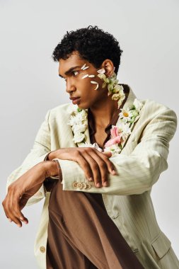 Genç Afrikalı Amerikalı bir adam şık bir ceketle poz veriyor, boynunda ve yüzünde çiçekler var..