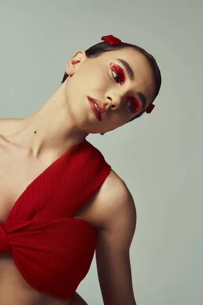 stock image A young woman with short hair poses in a red crop top and mini skirt against a grey background.