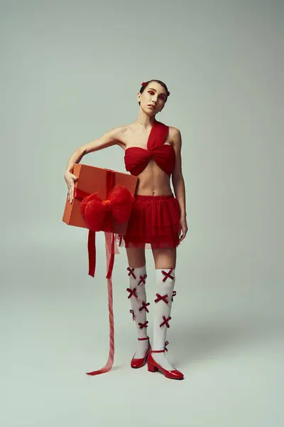 stock image A young woman with short hair poses in a red outfit, holding a large gift box with a bow.