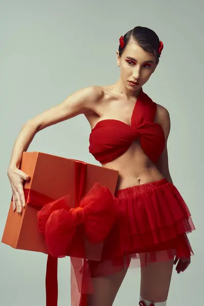 stock image A young woman in a red outfit with a bow holds a large, wrapped gift in a studio setting.