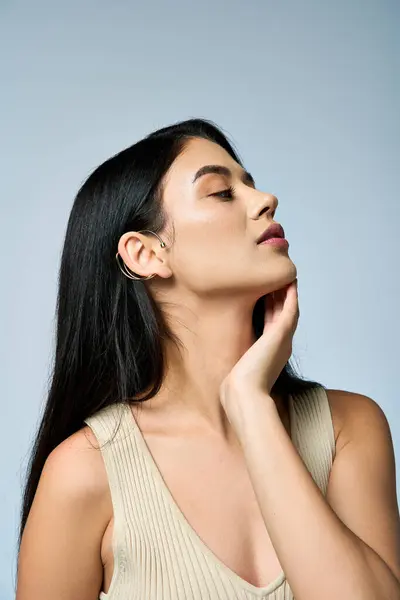 stock image A young woman with long black hair poses confidently while wearing a stylish, light-colored top.