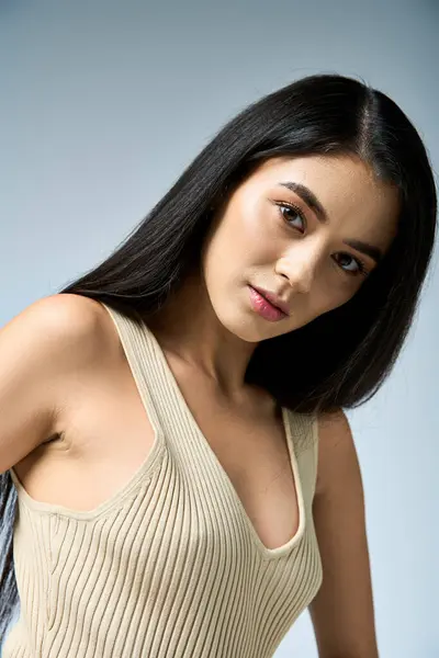 stock image A young woman with long black hair poses in a white tank top.