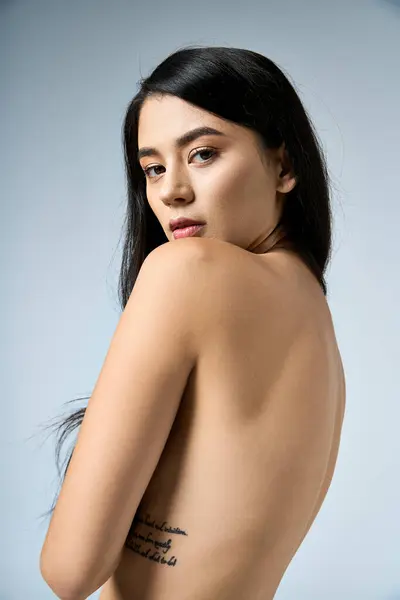 stock image Young woman in studio with long black hair, back to camera, gazes over shoulder.