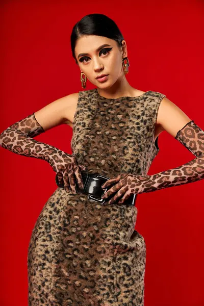 stock image A young woman poses in a leopard print dress and matching gloves against a red background.