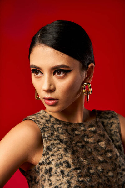 Женщина в леопардовом платье позирует на красном фоне, пристально смотрит.
