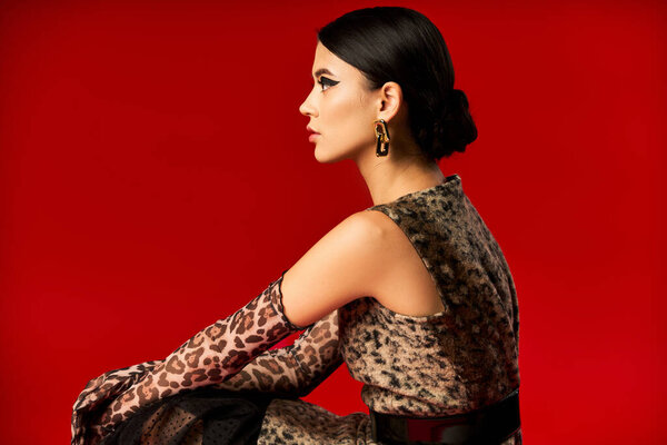 Молодая женщина в леопардовом платье позирует на красном фоне.