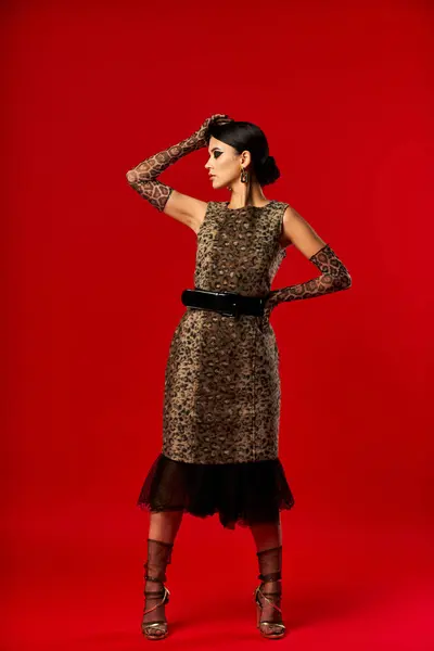 stock image A young woman poses in a leopard print dress and stylish gloves against a red background.