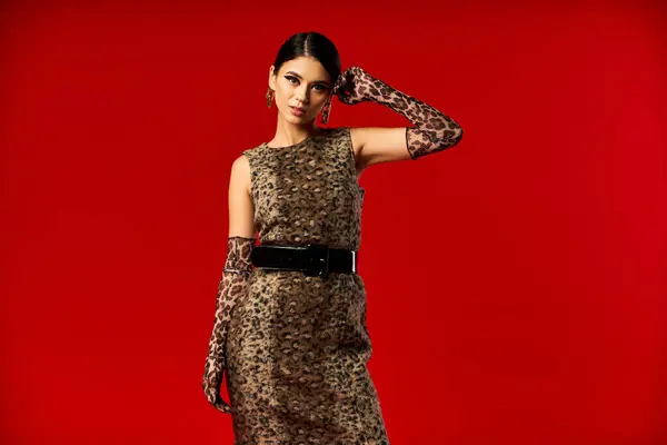 stock image A young woman in a leopard print dress and gloves poses against a red backdrop.