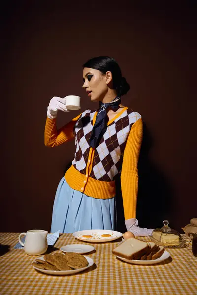 stock image A young woman in a yellow and brown cardigan drinks coffee at a table set with breakfast.