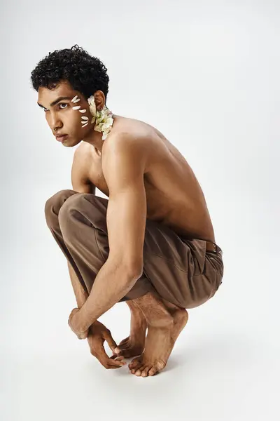 stock image A young, muscular African American man poses against a grey background, adorned with white flowers.