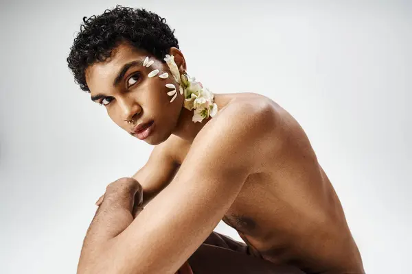 Stock image A young, muscular African American man poses with flowers adorning his body and face against a grey background.