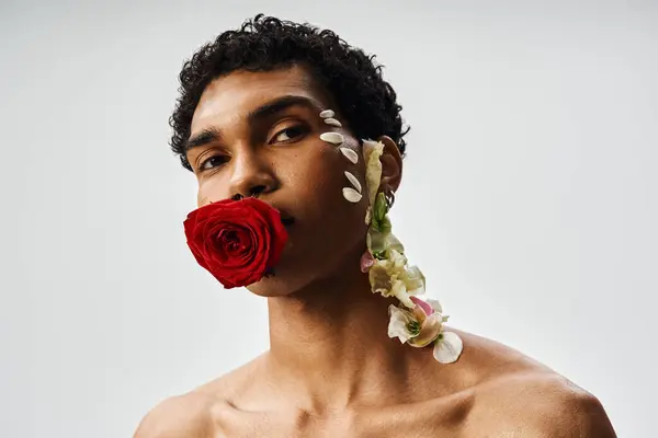 stock image A young, muscular African American man poses with flowers adorning his body and face against a grey backdrop.