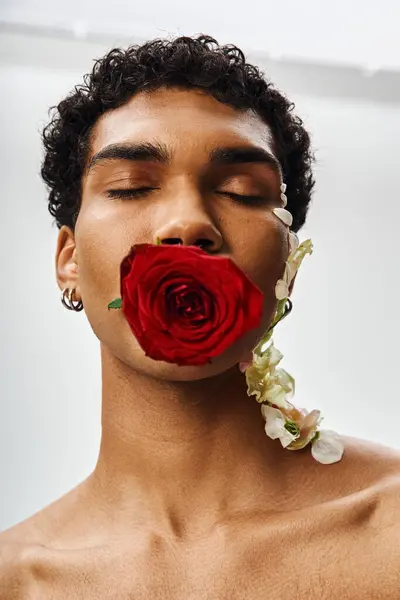 stock image A young, muscular African American man poses with a red rose covering his mouth, and white flowers adorning his face and neck.